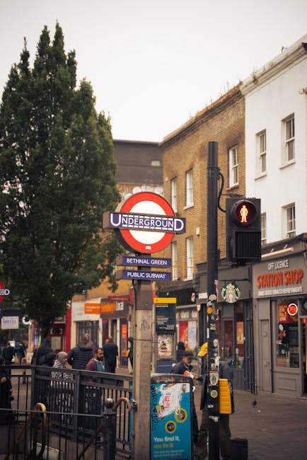 A busy London street scene at Bethnal Green featuring the iconic London Underground sign with a blue 'Bethnal Green' station plaque, surrounded by pedestrians waiting to cross at a traffic light displ